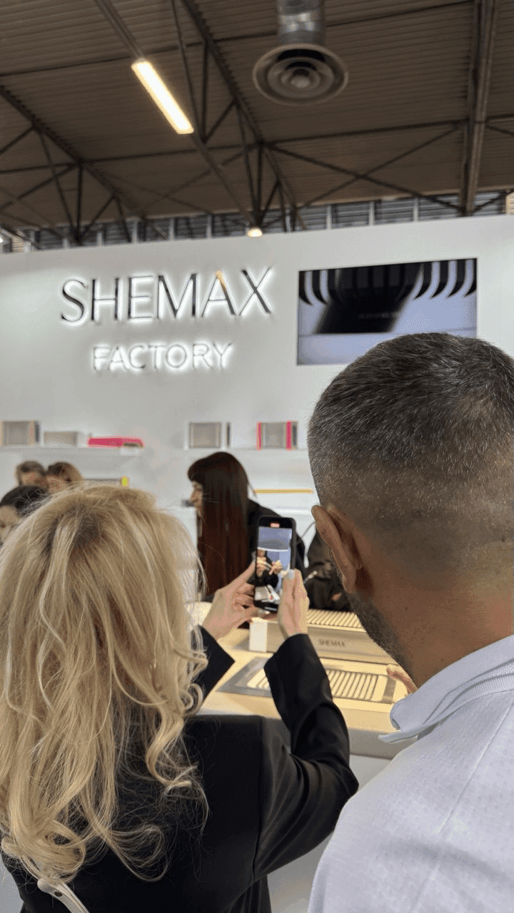 People take photos of a SHEWAX display booth with neon lighting.