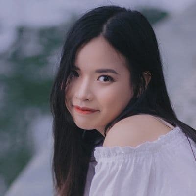 A young woman with long black hair and an off-the-shoulder top smiles gently.