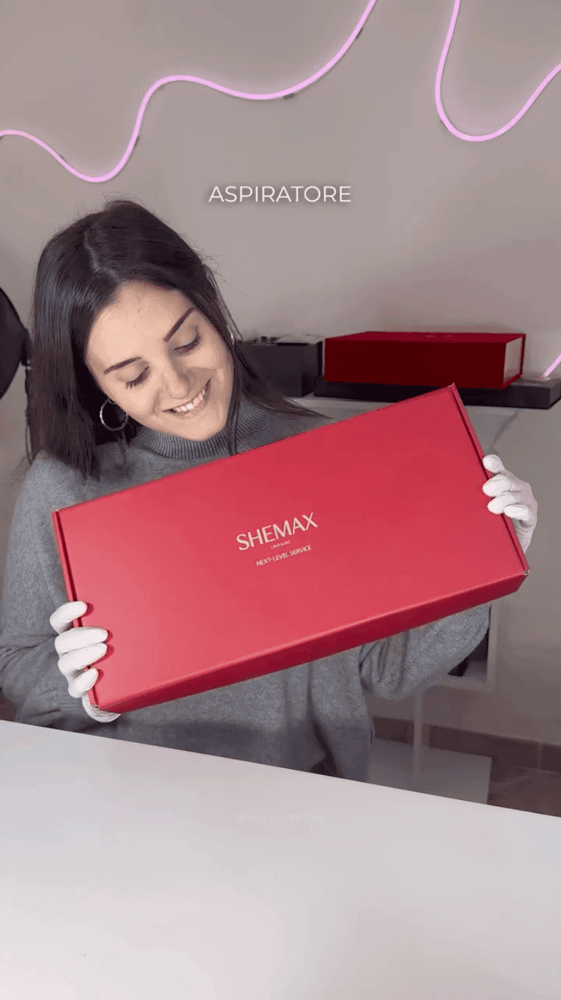 A smiling woman wearing white gloves holds a red box with gold lettering.