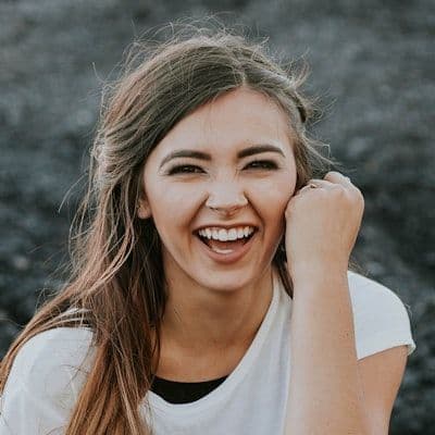 A young woman with brown hair laughs heartily, her hand near her face.